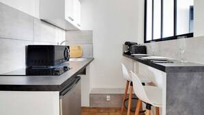 Une cuisine moderne équipée d’un four à micro-ondes, d’un grille-pain et d’une planche à découper en bois sur le plan de travail, ainsi que d’un évier et d’une fenêtre avec des stores.