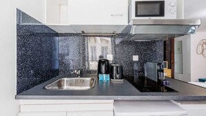 Una cocina moderna con salpicadero negro moteado, pileta de acero inoxidable y un microondas sobre la cocina.
