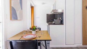 Cocina compacta con comedor, que incluye una mesa de madera preparada para dos comensales, un armario blanco y una estufa moderna.