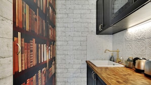 A kitchen with a brick wall, a wooden countertop, a sink with a gold faucet, and a decorative backsplash. - The Wizard's Studio! (Paris)