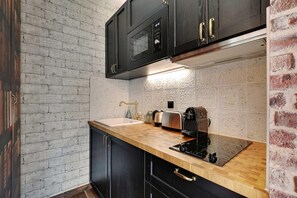 A kitchen with a brick wall, black cabinets, a wooden countertop, and a stainless steel toaster. - The Wizard's Studio! (Paris)