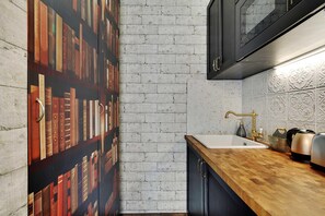 A kitchen with a brick wall, a wooden countertop, a sink, and a bookshelf with books. - The Wizard's Studio! (Paris)