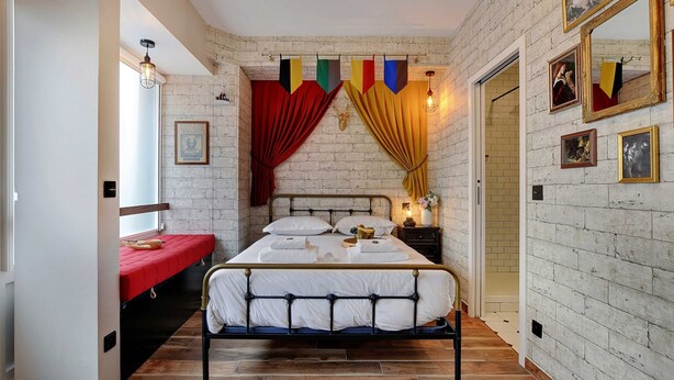 A bedroom with a bed, a window, a red curtain, a wooden floor, and a brick wall. - The Wizard's Studio! (Paris)