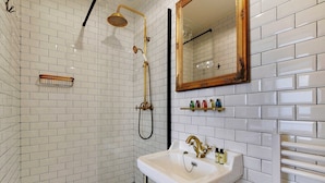A bathroom with white subway tiles, a gold-framed mirror, a white sink, and a gold showerhead. - The Wizard's Studio! (Paris)