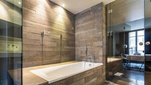 A modern bathroom with a large bathtub, glass shower enclosure, and a view of the city through a large window. - Modern Apartment - 1br/4p - Passy (Paris)