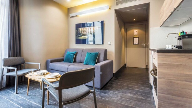 A modern living room with a sofa, chairs, a small table, and a kitchen area with a counter and sink. - Modern Apartment - 1br/4p - Passy (Paris)