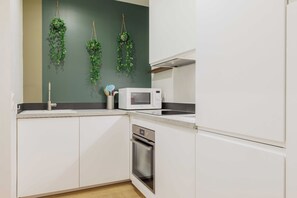 A kitchen with white cabinets, a microwave, and a stainless steel oven. - Authentic Studio - 2P - Eiffel Tower (Paris)