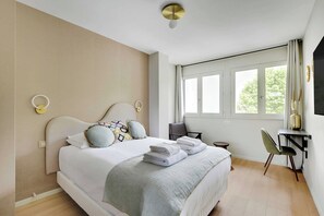 Un dormitorio moderno con una cama grande, mesitas de noche, un escritorio y una ventana con cortinas.