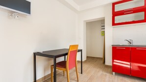 Une petite cuisine avec un meuble rouge, une table noire et une chaise en bois.