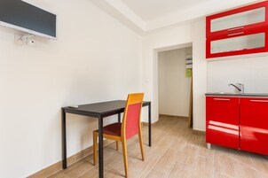 Una pequeña cocina con un armario rojo, una mesa negra y una silla de madera.