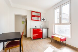 Cocina compacta con un mueble rojo, microondas y un lavamanos pequeño. Hay una mesa de comedor con una silla y un banco cerca de la ventana.