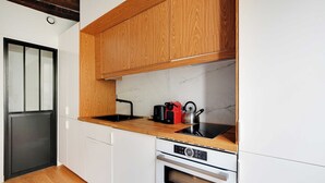 A compact kitchen with wooden cabinets, a black induction cooktop, a red kettle, and a Bosch oven. - Chic Studio A/C - 2P - Le Marais (Paris)