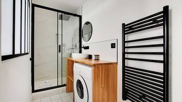 Une salle de bain moderne dotée d’une douche à parois de verre, d’un lave-linge et d’un meuble-lavabo en bois avec un évier et un miroir.