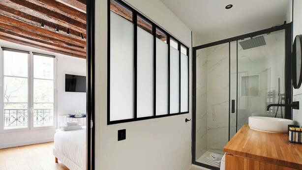 A modern hotel room with a large bed, a wooden ceiling, a glass shower enclosure, and a wooden vanity with a sink. - Chic Studio A/C - 2P - Le Marais (Paris)