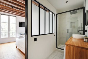 A modern hotel room with a large bed, a wooden ceiling, a glass shower enclosure, and a wooden vanity with a sink. - Chic Studio A/C - 2P - Le Marais (Paris)