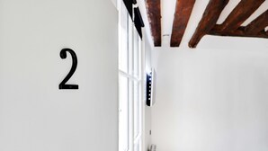 A room with a white wall, a number '2' sign, a window with blinds, and a radiator. - Chic Studio A/C - 2P - Le Marais (Paris)