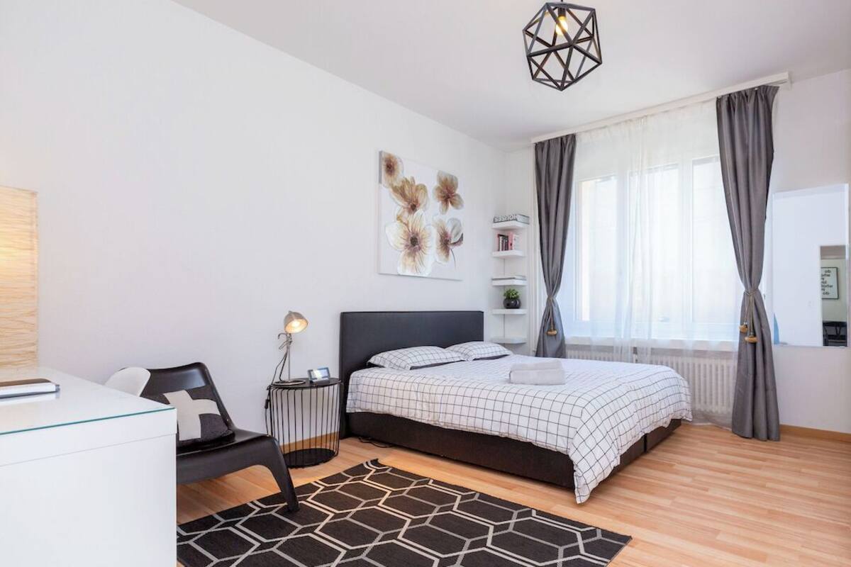 Quarto moderno com cama, mesas de cabeceira, escrivaninha e luminária.