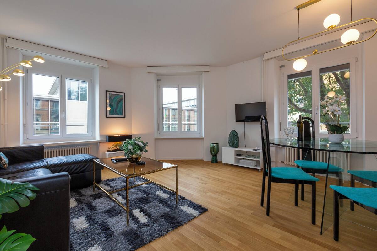Uma sala de estar moderna com uma mesa de jantar de vidro, sofá de couro preto e um tapete preto e branco.