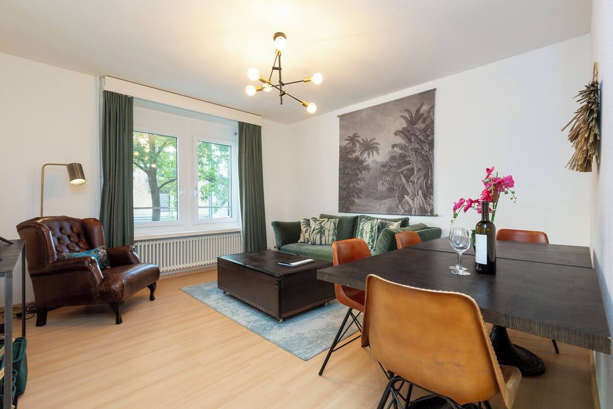 Uma sala de estar moderna com sofá, mesa de centro, mesa de jantar com cadeiras, abajur e uma grande pintura na parede.