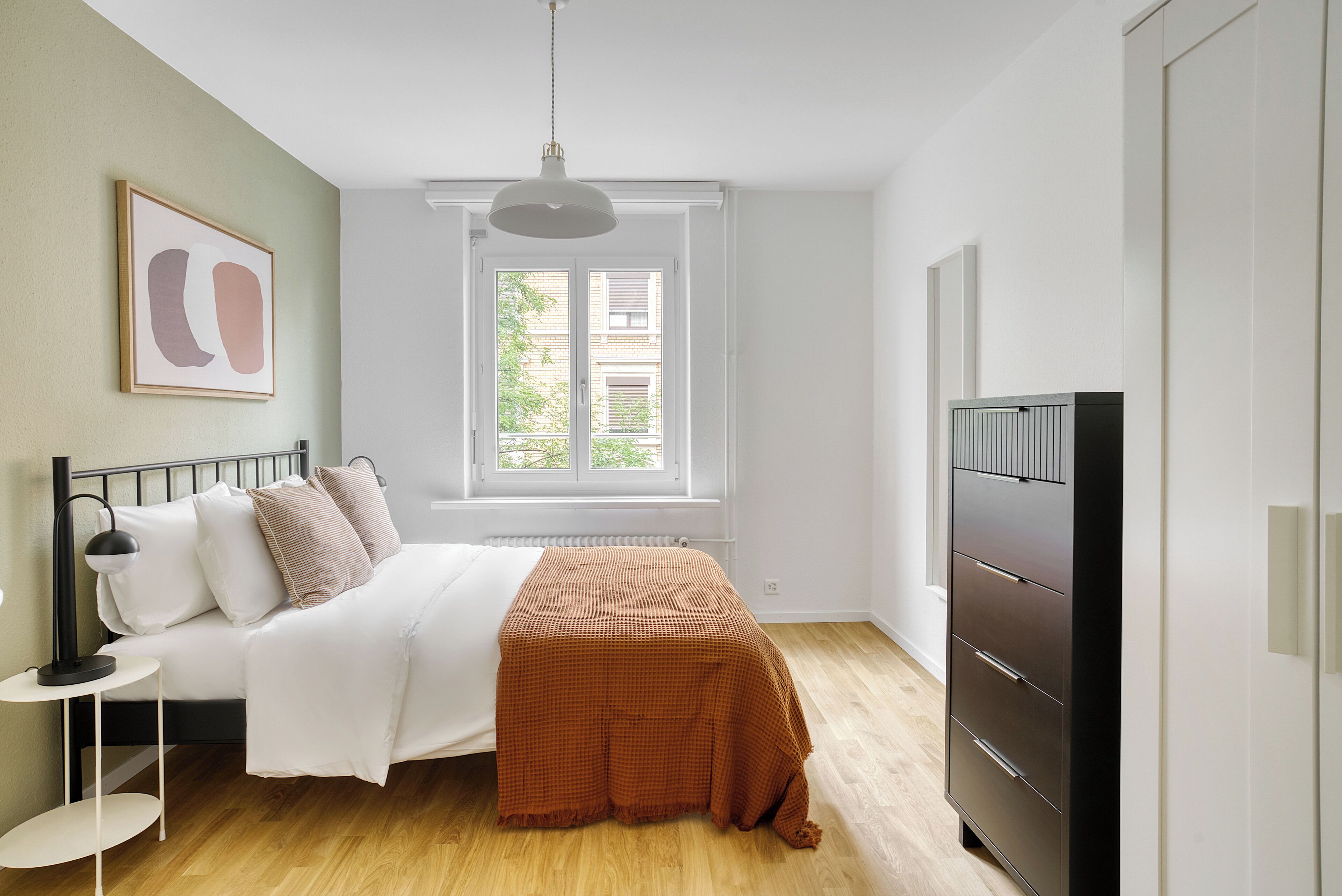 Quarto com cama, mesa de cabeceira, abajur, cômoda, janela e obras de arte.