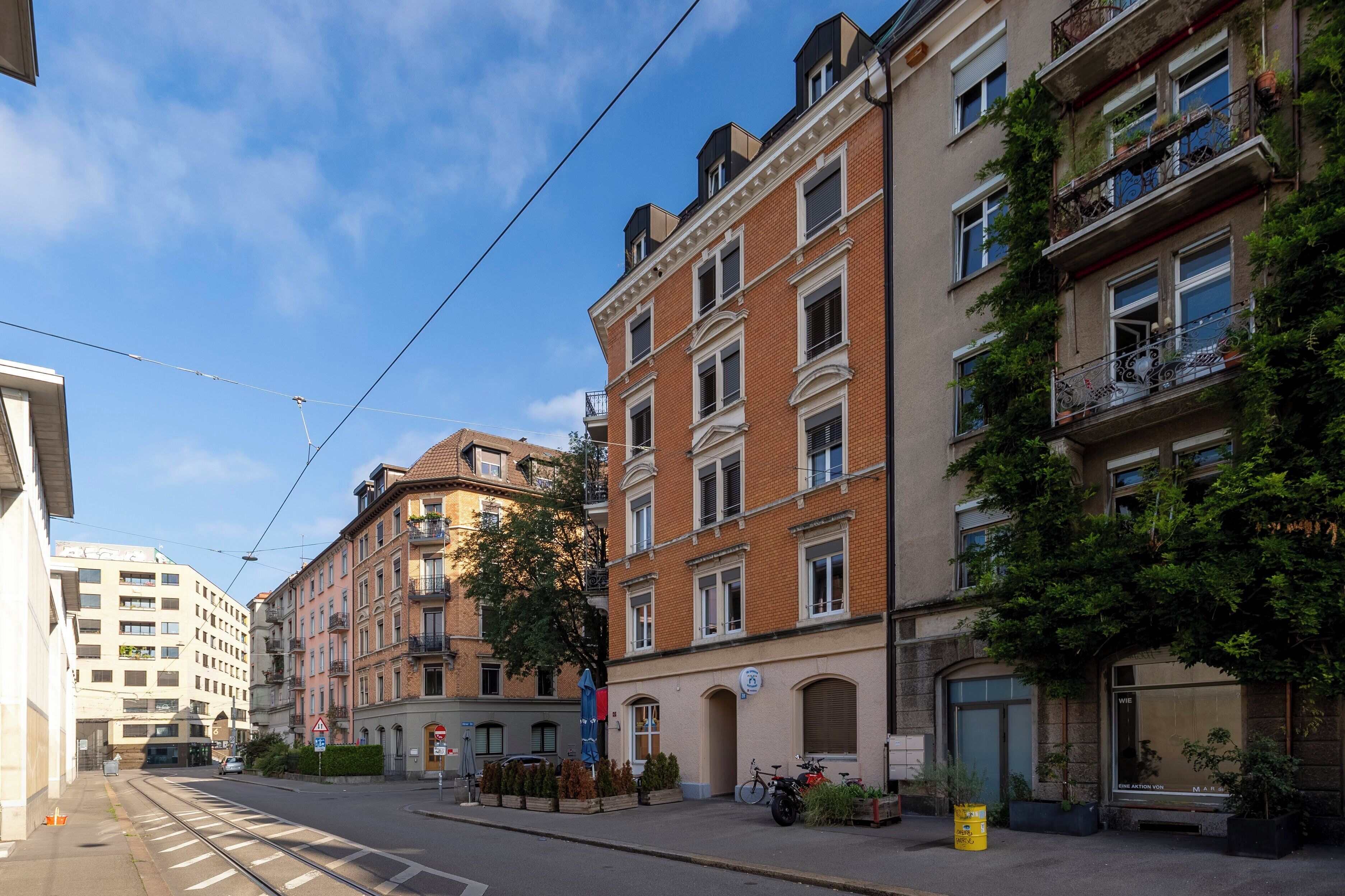 A street view with multi-story buildings, a tram line, and a clear sky.