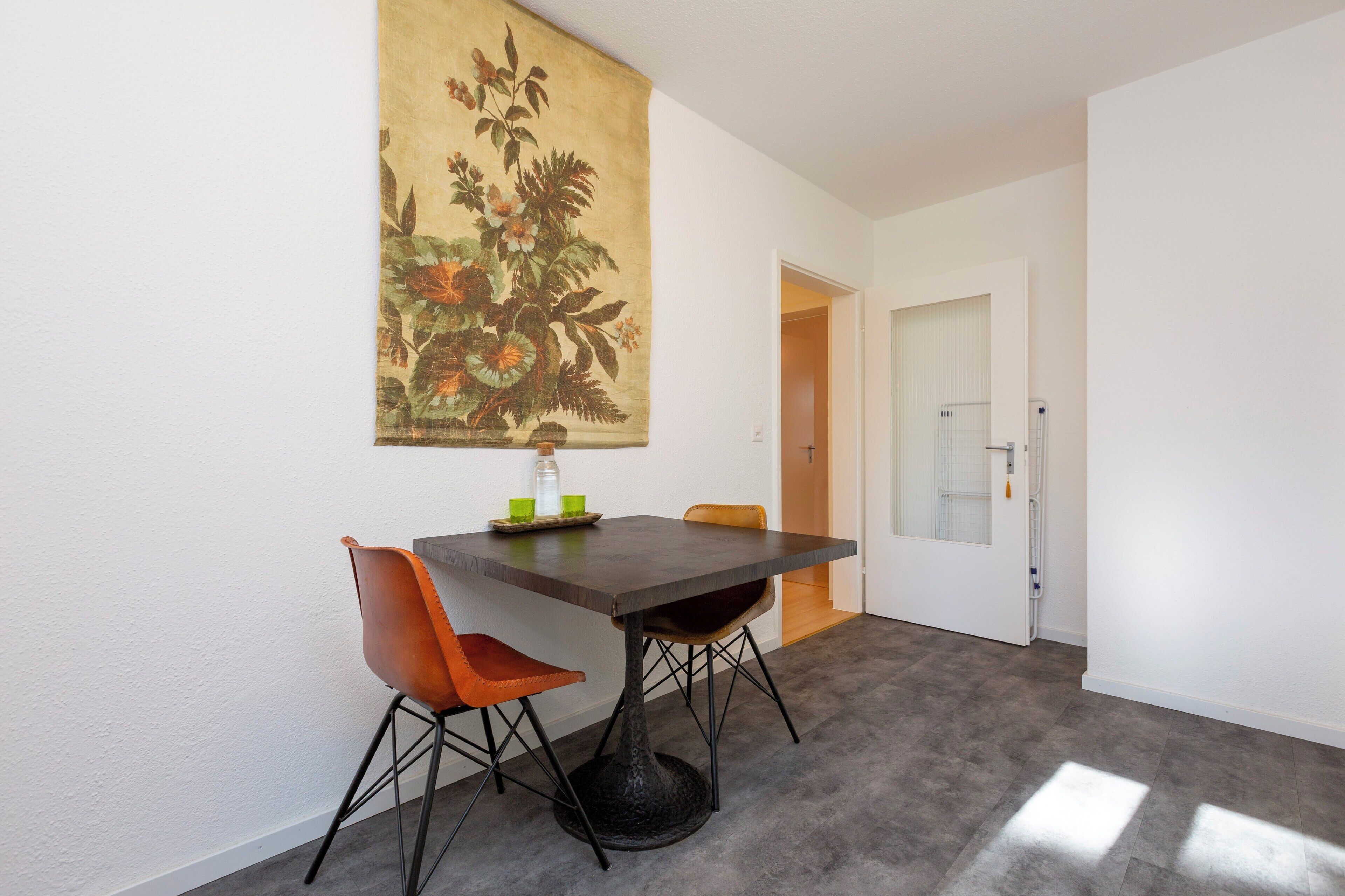 Un comedor con mesa y sillas, un cuadro en la pared y una puerta que da a otra habitación.