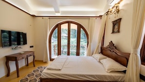 A bedroom with a large bed, a TV, a wooden desk, and a view through a window. - Ishaan Holiday Home (Alibag)