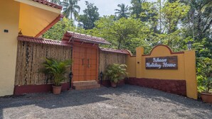 A gated entrance to a property named 'Isaan Holiday Home' with a red door, a bamboo fence, and potted plants. - Ishaan Holiday Home (Alibag)