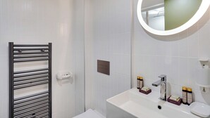 Un baño moderno con un lavamanos blanco, un espejo con marco circular y un perchero para toallas.