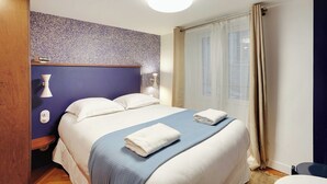 Habitación de hotel con una cama grande, una mesita de noche, una lámpara y una ventana con cortinas.