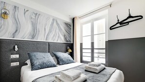 A modern bedroom with a marble-patterned headboard, a neatly made bed with folded towels, and a window with a view. - Cosy Studio With Air Conditioning -near Montmartre (Paris)