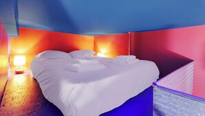 Een keurig opgemaakt bed met witte lakens in een kamer met blauwe en oranje wanden.