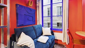 Een kamer met een blauwe bank, een klein houten tafeltje en een raam met blauwe gordijnen.