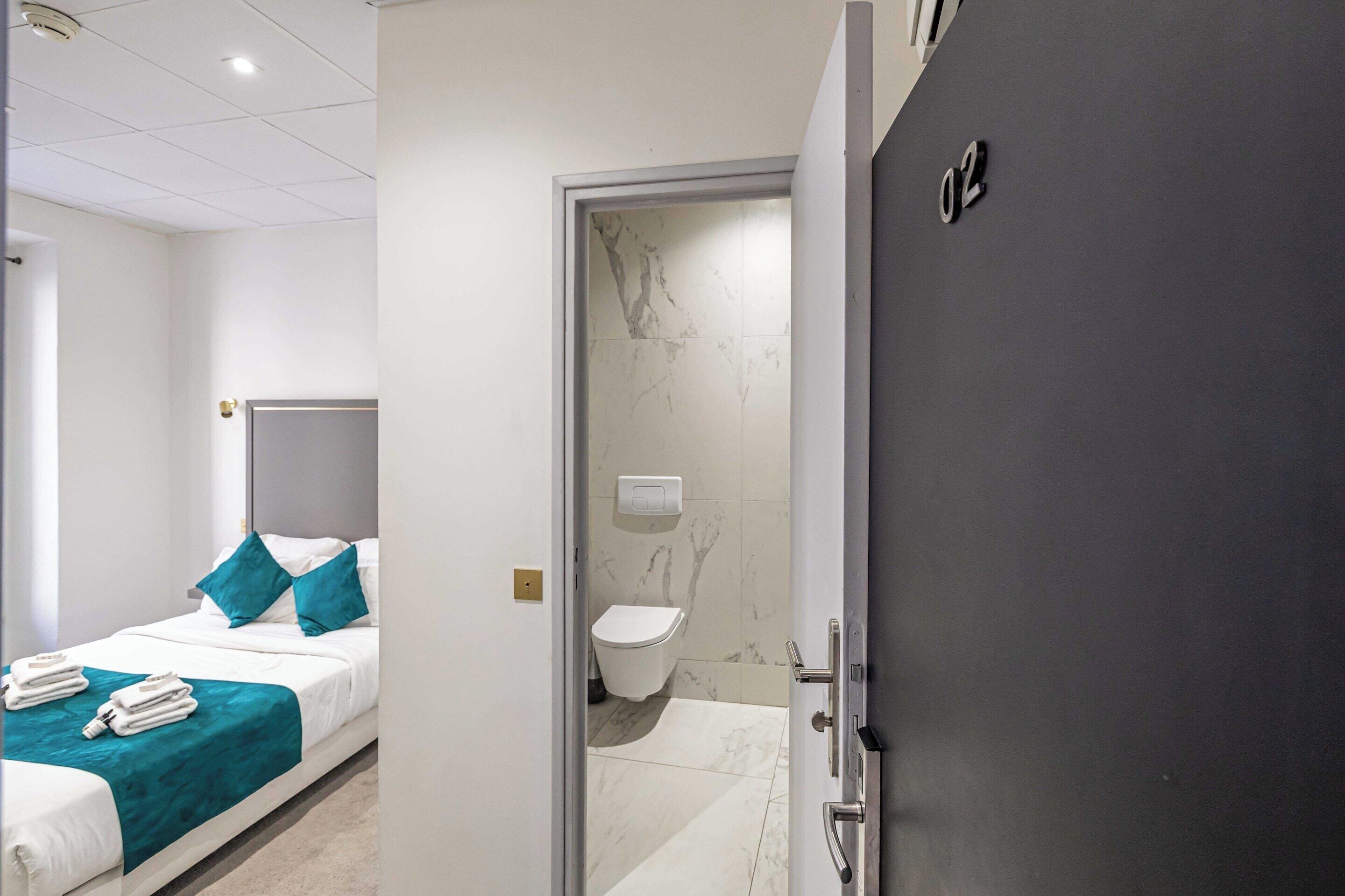 A hotel room with a bed, a bathroom with a toilet and a shower, and a door with a number.
