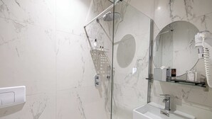 Ein modernes Badezimmer mit einer gläsernen Dusche, einem weißen Waschbecken und einem Spiegel mit runder Reflexion.