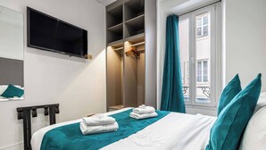 Ein Hotelzimmer mit Bett, Fernseher, Schrank und einem fensterbepflanzten Fenster.