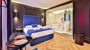 A modern hotel room with a large bed, a sitting area with a table and chairs, a glass-enclosed shower area, and a marble-tiled bathroom. - Wonderful Private Room - 2P - Chatelet (Paris)