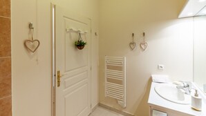 A bathroom with a white door, a towel rack with a plant, a towel rack with a heart-shaped decoration, a white radiator, and a sink with a mirror. - Cosy Studio - 2P - Port de Deauville (Deauville)