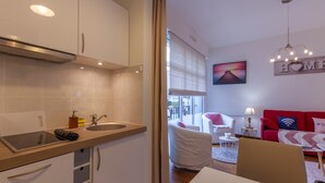 A modern kitchen with a sink, countertop, and cabinets. There is a dining area with a table and chairs, and a red sofa with a cushion. A painting is on the wall, and a sign with the word "HOME" is visible. - Cosy Studio - 2P - Port de Deauville (Deauville)