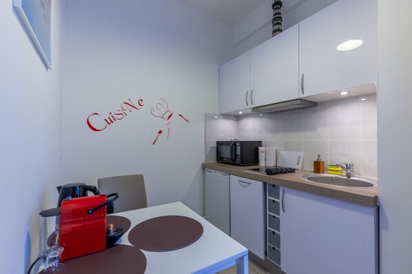 A compact kitchen with white cabinets, a microwave, a sink, and a table with two chairs. - Cosy Studio - 2P - Port de Deauville (Deauville)