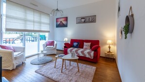 A living room with a red sofa, white armchairs, a round coffee table, and a view through large windows. - Cosy Studio - 2P - Port de Deauville (Deauville)