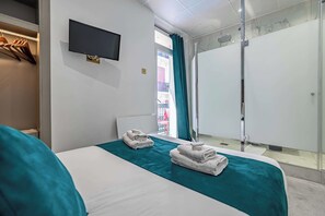 A hotel room with a bed, a TV, a bathroom with a shower, and a balcony with a view.