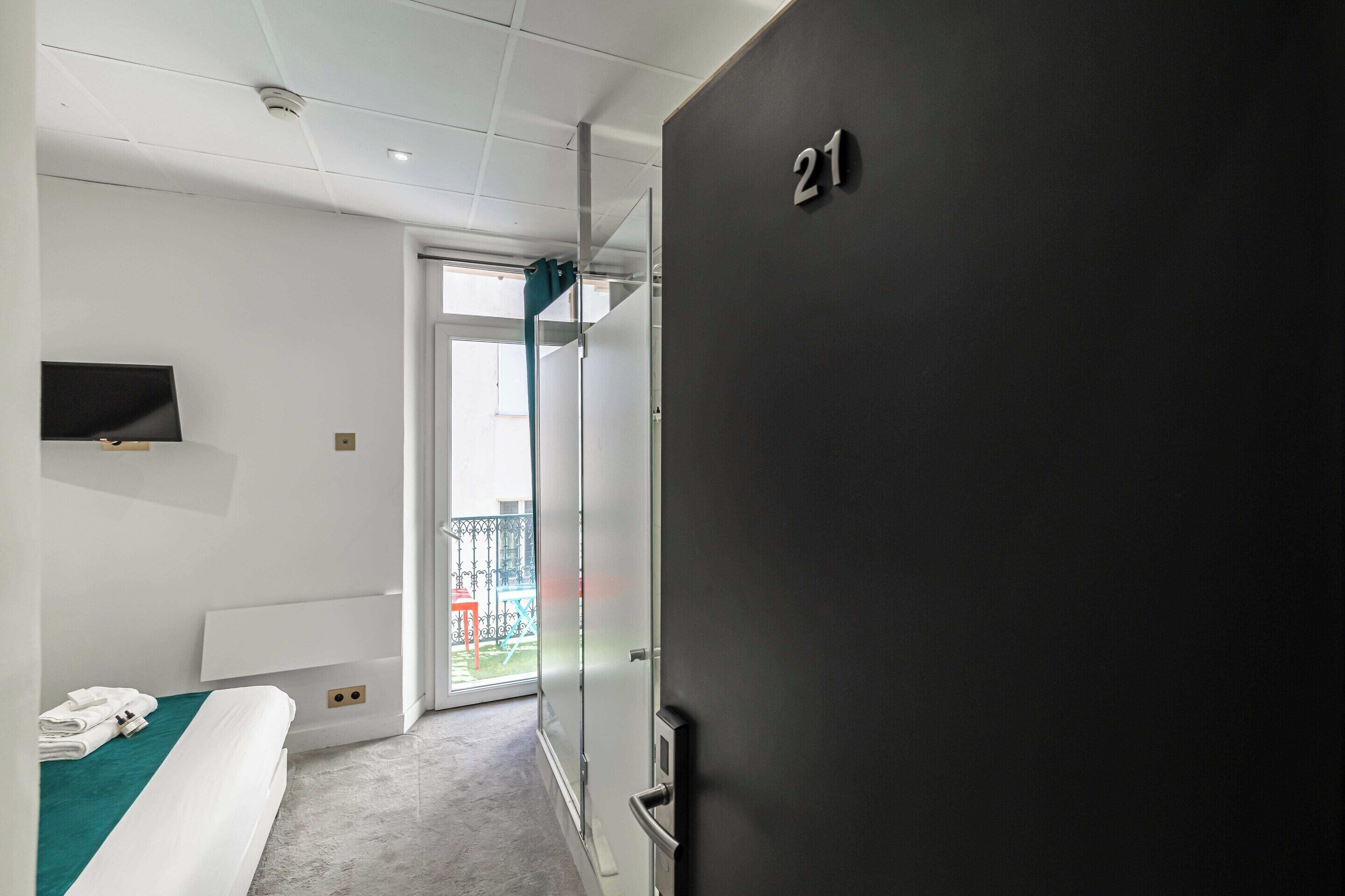 Une chambre d’hôtel moderne équipée d’un lit, d’une télévision, d’un balcon et d’une porte portant le numéro 21.