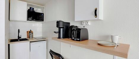 A compact kitchen with a microwave, coffee maker, toaster, and a small dining area with a chair and a cup.