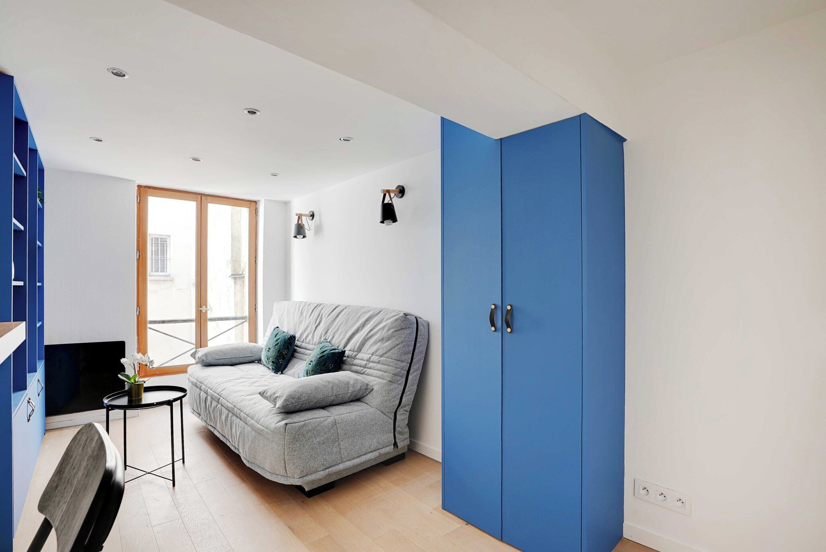 A compact living space with a grey sofa, a small round table, and a blue wardrobe.