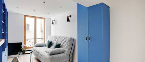 A compact living space with a grey sofa, a small round table, and a blue wardrobe.
