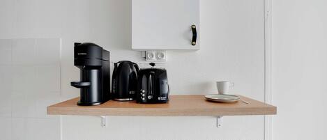 Une petite cuisine équipée d’une machine à café, d’une bouilloire et d’une tasse, le tout posé sur un plan de travail en bois.