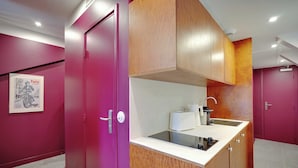 A compact kitchen with a built-in sink, wooden cabinets, and a pink door. - Elegant Studio - 2P - Republique (Paris)