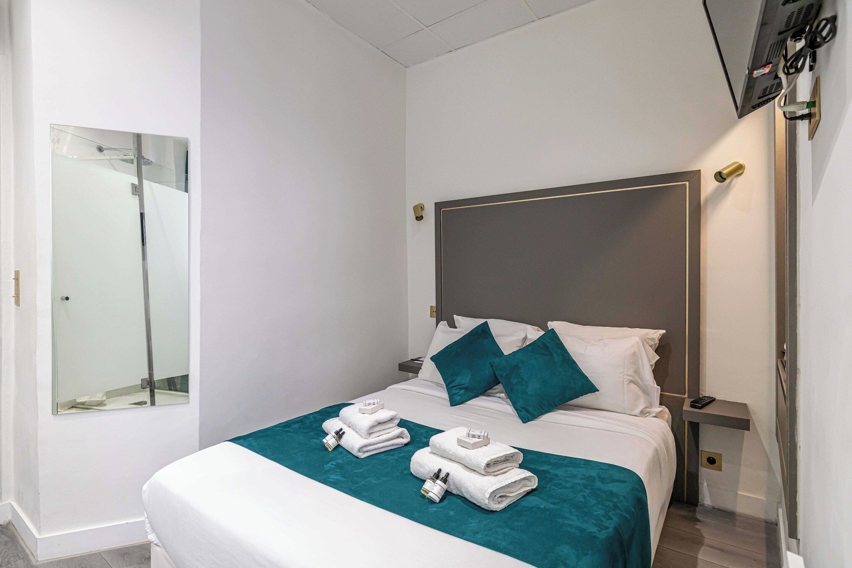 Una camera d'albergo con un letto, un comodino, una televisione e uno specchio.