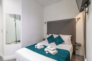 Una habitación de hotel con una cama, una mesita de noche, un televisor y un espejo.